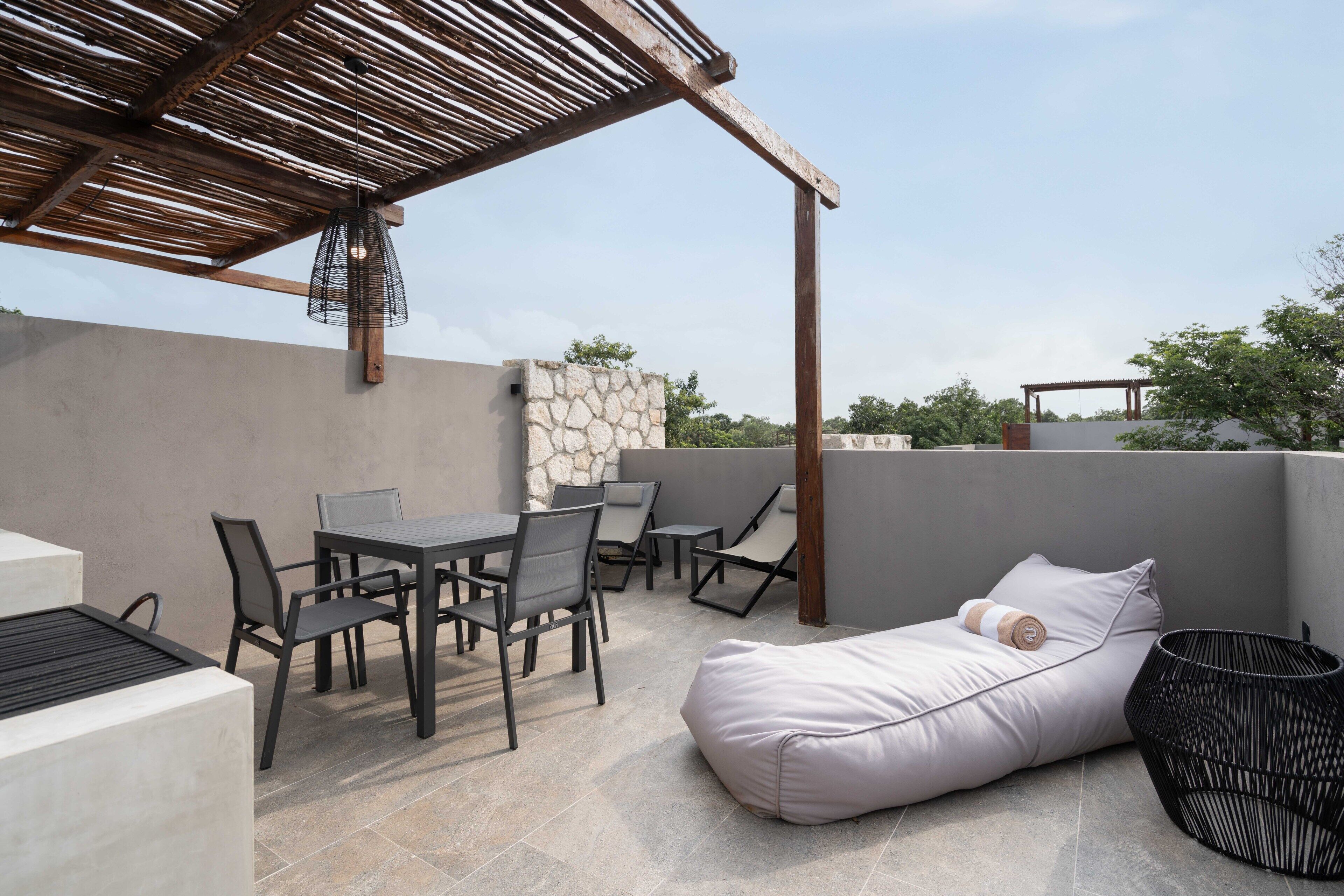 An outdoor patio with a table and chairs, a cushioned seating area, and a stone wall.
