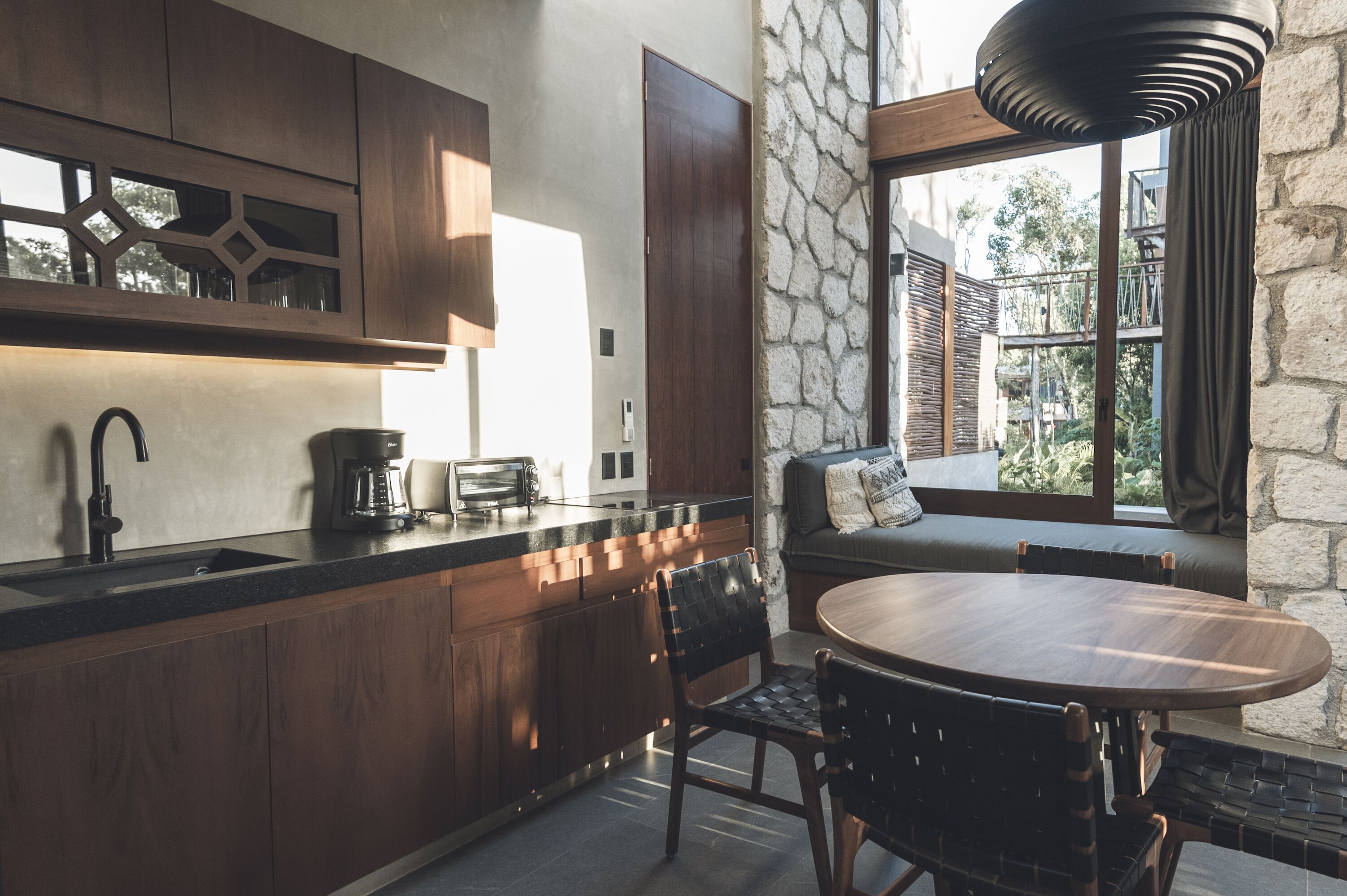 A modern kitchen with dark wood cabinets, a built-in oven, and a stone wall.