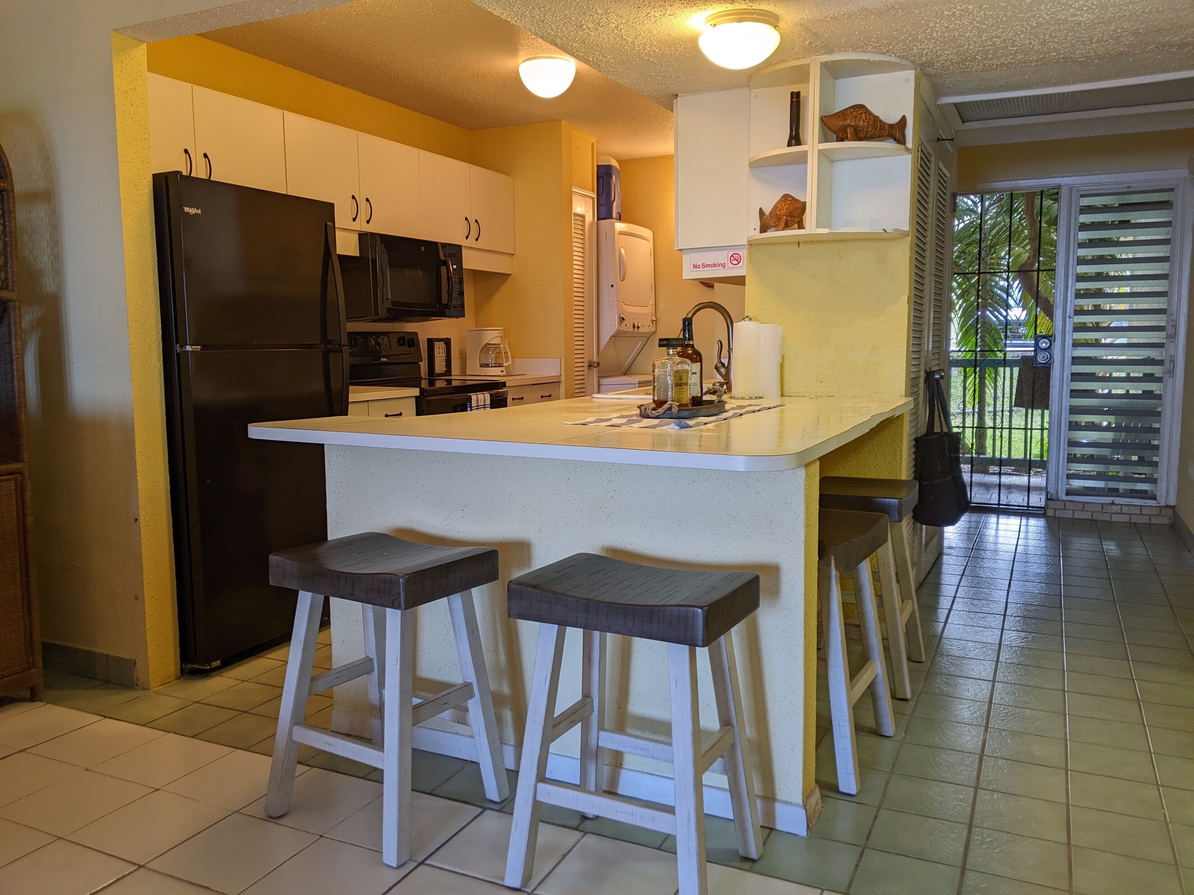 A kitchen with a central island, bar stools, a refrigerator, microwave, and a coffee maker.