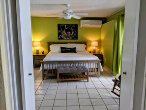 A bedroom with a bed, nightstands, a ceiling fan, and a wall-mounted air conditioner. - Walk out to Sugar beach (Christiansted)