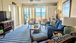 A living room with a blue sofa, a coffee table, a TV, and a balcony with chairs. - Walk out to Sugar beach (Christiansted)