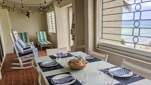 A dining area with a table set for four, including plates, cutlery, and glasses. There are two rocking chairs and a striped chair near a window with a view of the sea. - Walk out to Sugar beach (Christiansted)