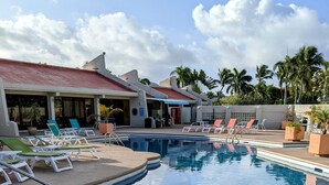 A pool area with lounge chairs and a building with a red roof. - Walk out to Sugar beach (Christiansted)