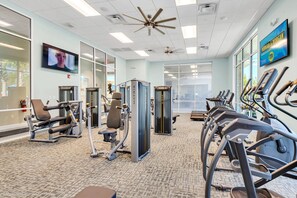 Een sportschool met fitnessapparatuur, een televisie en een plafondventilator.