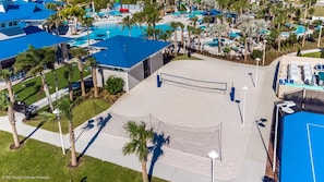 An aerial view of a resort with multiple swimming pools, palm trees, and a tennis court.