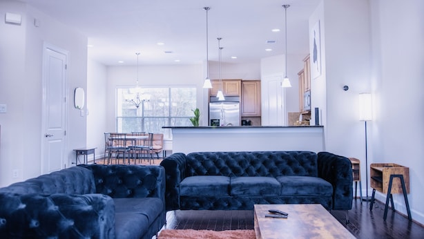 Un salon moderne avec un canapé d’angle bleu foncé, une table basse en bois et un coin repas comprenant une table et des chaises.
