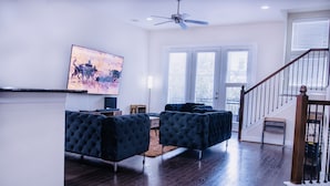 Un vaste salon doté d’un parquet en bois foncé, d’un grand canapé bleu foncé, d’un ventilateur de plafond et d’un tableau accroché au mur.