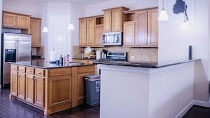Une cuisine moderne avec des meubles en bois, des appareils électroménagers en acier inoxydable et des luminaires suspendus.