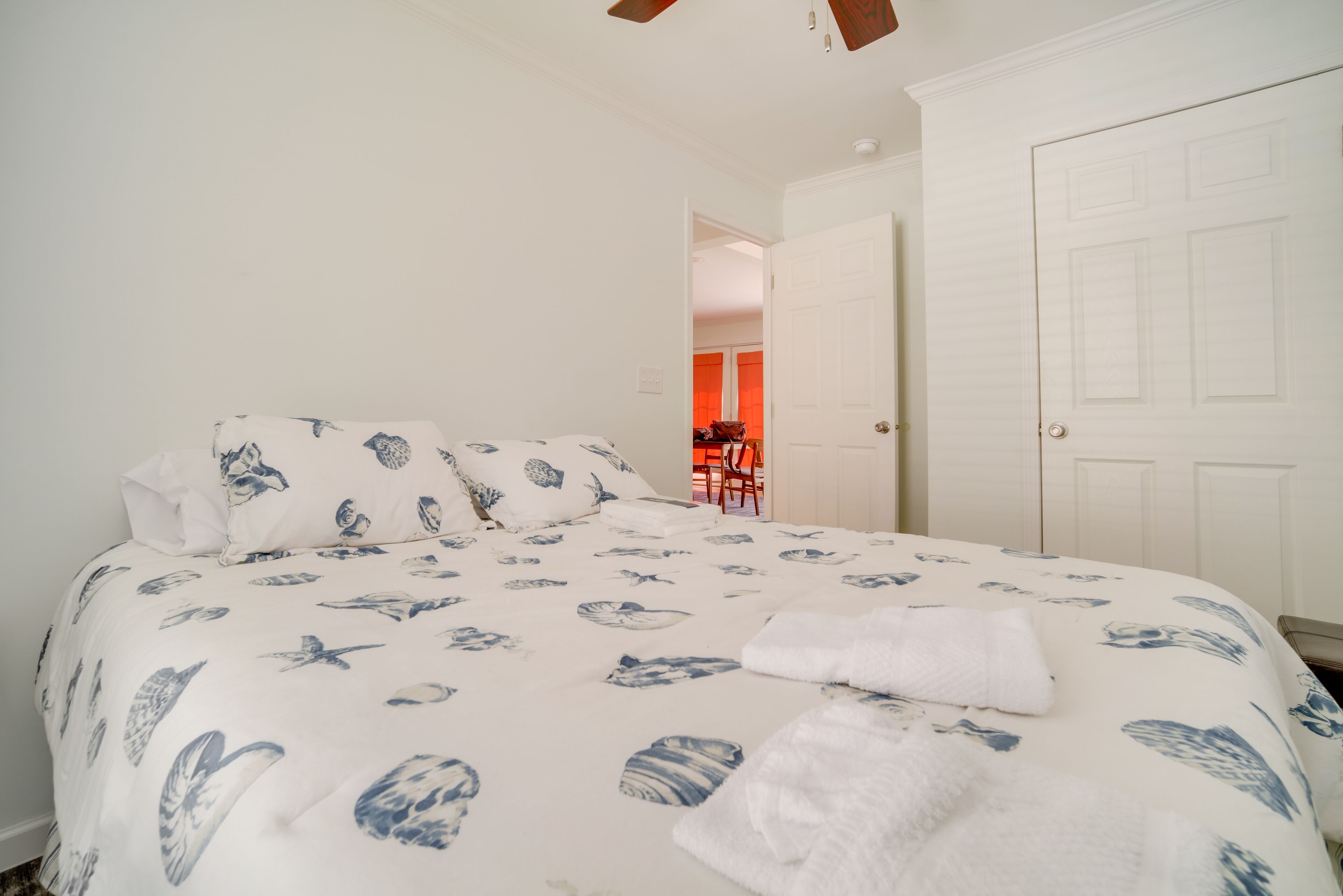 A bedroom with a bed, white walls, and a door leading to another room.