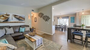 A living room with a sectional sofa, a coffee table, and a dining area with a table and chairs. - Lovely Morehead City Home w/ Fire Pit & Gas Grill (Morehead City)