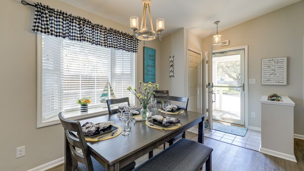 A dining area with a wooden table set for four, a chandelier, and a view of the outdoors through a glass door. - Lovely Morehead City Home w/ Fire Pit & Gas Grill (Morehead City)