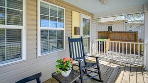 A covered porch with a rocking chair, a potted plant, and a view of a wooden fence and house in the background. - Lovely Morehead City Home w/ Fire Pit & Gas Grill (Morehead City)