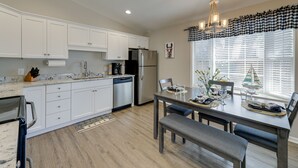 A modern kitchen with white cabinets, stainless steel appliances, and a dining area with a table set for four. - Lovely Morehead City Home w/ Fire Pit & Gas Grill (Morehead City)