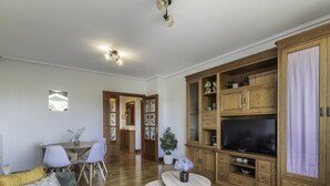 Un salon spacieux doté d’un plancher en bois, d’un canapé, d’une table à manger avec des chaises, d’un téléviseur et d’un meuble avec des portes en verre.