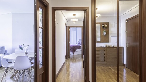 Un couloir avec un plancher en bois, un coin repas avec des chaises blanches et une cuisine avec des meubles en bois.