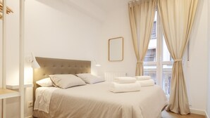 Quarto bem organizado com uma cama grande, abajures e vista para o exterior através de uma janela com cortinas.