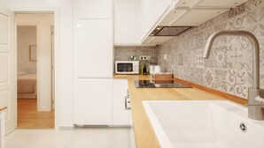 Uma cozinha moderna com armários brancos, bancada de madeira, micro-ondas embutido e pia com torneira moderna.