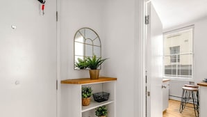 Un couloir étroit, dans lequel se trouve une étagère en bois portant un pot de fleurs et des paniers noirs.