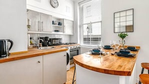 Une cuisine moderne avec des meubles blancs, un plan de travail en bois et un coin repas agrémenté d’une vaisselle et de verres bleus.
