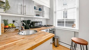 Une cuisine moderne avec des meubles blancs, un plan de travail en bois, un évier, une cuisinière, un four à micro-ondes et une fenêtre avec des stores.
