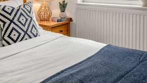 Une chambre à coucher avec un lit, une table de chevet avec une lampe, une fenêtre donnant sur un jardin et un radiateur.
