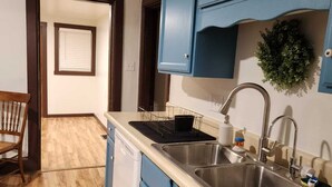 A kitchen with blue cabinets, a stainless steel sink, and a wooden floor. - Family Home in Carthage (Carthage)