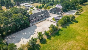 En vy från ovan av ett stort, öppet område med flera byggnader, omgivet av grönska och åkrar.