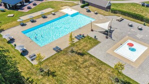 En vy från ovan av ett poolområde med en rektangulär pool, solstolar runt omkring och en avskärmad sittplats.