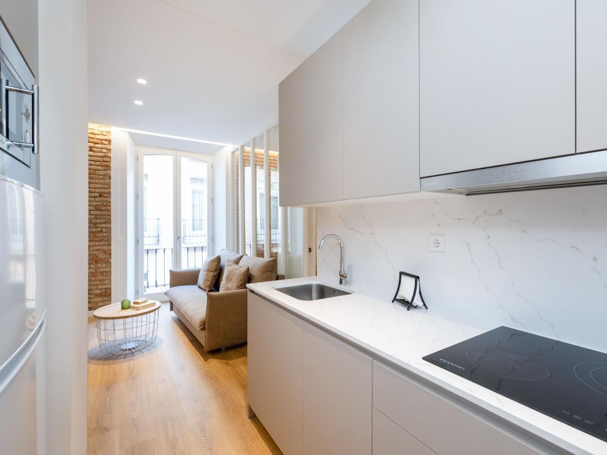 Una cocina moderna con estufa integrada, un lavamanos y una zona de comedor con sofá y una mesa redonda pequeña.
