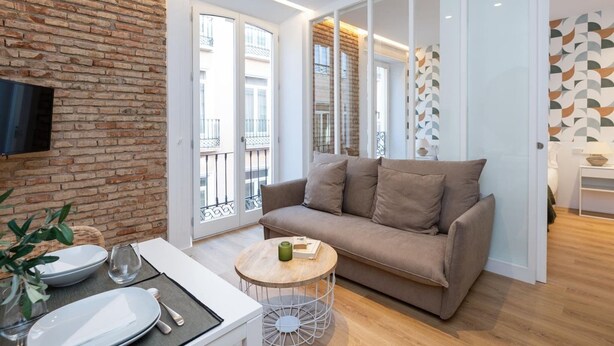 Una sala de estar moderna con pared de ladrillo, un sofá, una mesa de centro y un televisor montado en la pared.