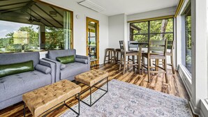 A spacious living room with a grey sofa, a brown ottoman, and a dining area with wooden chairs and a table. - 🌟Private🌟Views🌟x2KingSuites🌟HotTub🌟FirePit🌟NationalPark🌟SunSet🌟 (Sevierville)