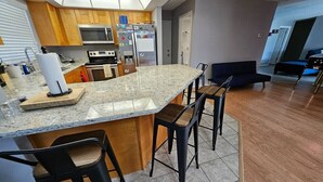 Moderni keittiö, jossa on graniittitaso, puukaapit, sisäänrakennettu uuni ja jääkaappi. Keittiössä on neljä baarituolia ja ruokapöytä.