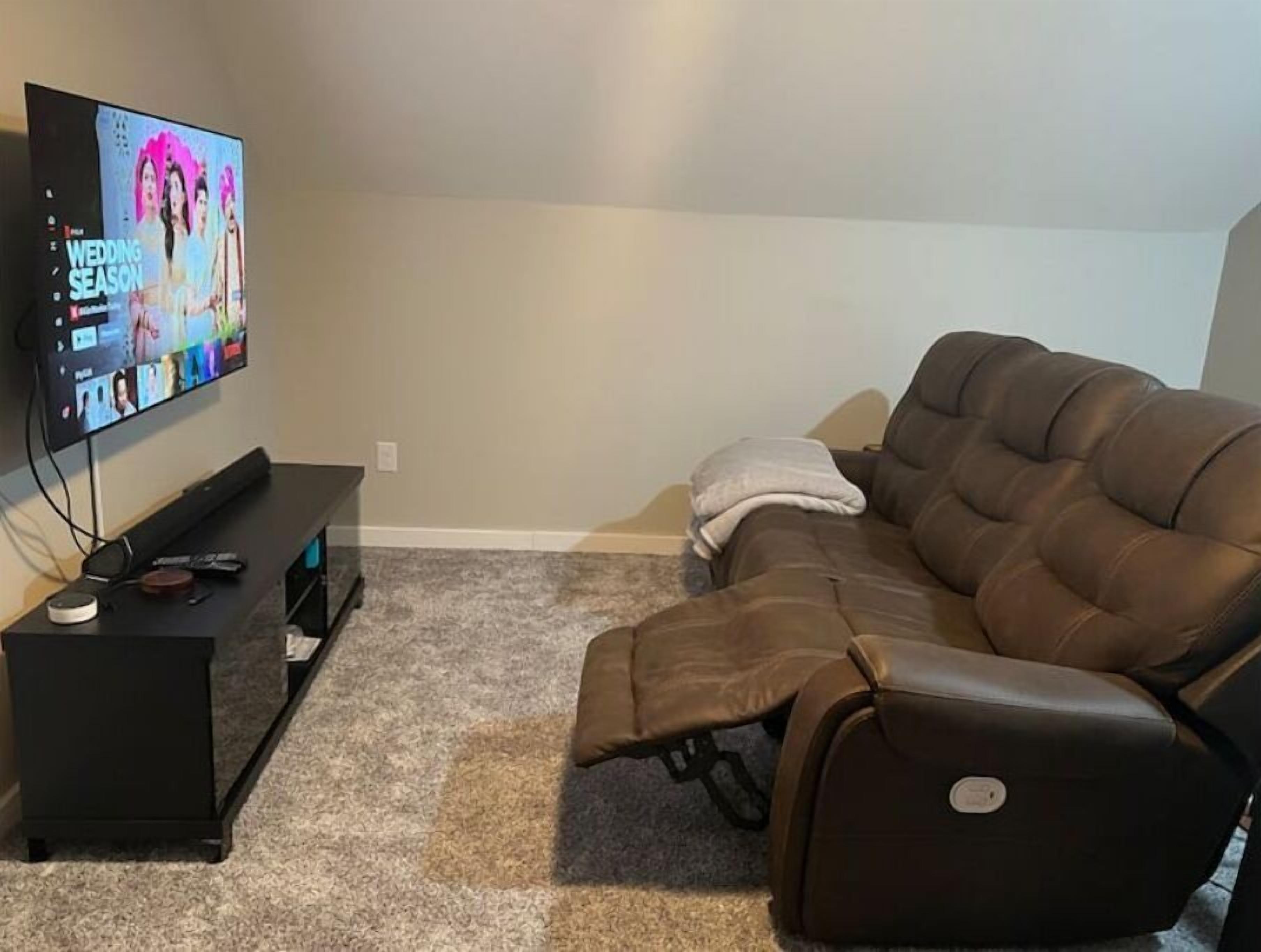 Ett vardagsrum med en stor TV med platt skärm som står på ett TV-bord, en brun lädersoffa och ett litet svart sidobord.