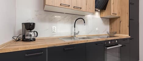 Una cocina moderna con una paleta de colores negro y madera, que incluye una cafetera, lavamanos y horno empotrado.