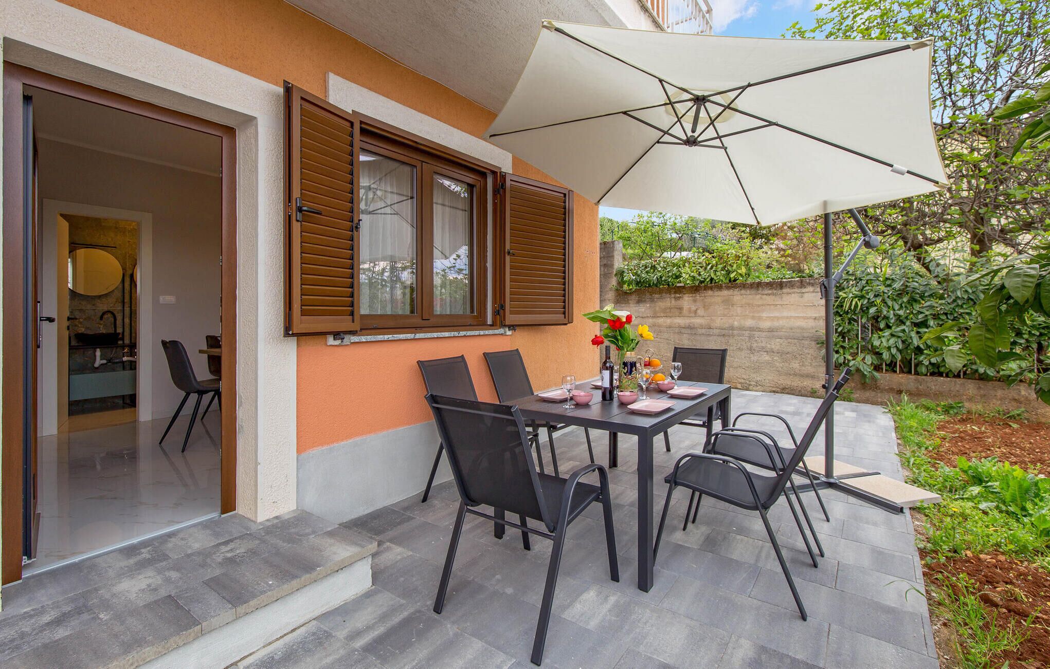 An outdoor patio with a table set for dining, surrounded by chairs, and an umbrella providing shade.
