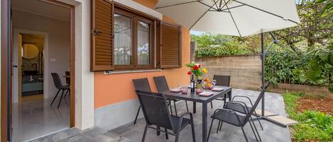 An outdoor patio with a table set for dining, surrounded by chairs, and an umbrella providing shade.