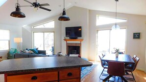A spacious kitchen with a large island, wooden cabinets, and a fireplace. There is a dining area with a table and chairs, and a television mounted above the fireplace. - Lakefront Cabin Hot Tub Playground Fire Pit (Algoma)