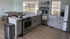 A modern kitchen with a central island, built-in appliances, and large windows offering views of the outdoors. - Private, newly renovated lakefront cottage on 10+ acres of land. (Brooklyn)