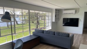 A modern living room with a grey sofa, a bench, and a TV mounted on the wall. - Private, newly renovated lakefront cottage on 10+ acres of land. (Brooklyn)