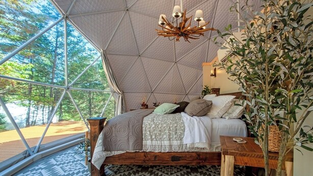 Een knus slaapkamer met een groot bed, een houten hoofdbord en uitzicht op bomen door een geometrisch raam.