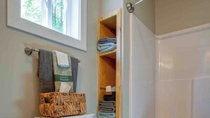 Een badkamer met een toilet, een rieten mand op de tank, een houten plank met handdoeken en een bad met een handdoek.