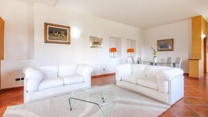 A living room with two white sofas, a glass coffee table, and a dining area with a table and chairs. - 4 bedroom stunning home in Roccadaspide (Roccadaspide)