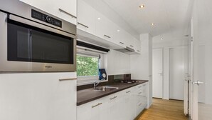 Een moderne keuken met een ingebouwde magnetron, roestvrijstalen apparatuur en een raam met uitzicht op groen.