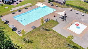 Luchtbeeld van een zwembadgedeelte met een rechthoekig zwembad, omringd door ligbedden en parasols, en een kleine tuin met een paddenstoelvormige decoratie.