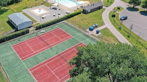 Luchtbeeld van een sportcomplex met een tennisbaan, een zwembad en een klein gebouw.