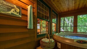 A wooden cabin interior with a hot tub, a sign requesting no floozies in the jacuzzi before 9:00pm, and a basket of towels.