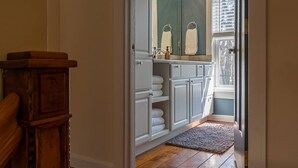 A bathroom with white cabinets, a mirror, and a window with blinds. - Saugatuck Cottage Steps from Downtown! (Saugatuck)
