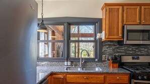 A kitchen with wooden cabinets, a granite countertop, a stainless steel sink, a microwave, and a stove. - Saugatuck Cottage Steps from Downtown! (Saugatuck)