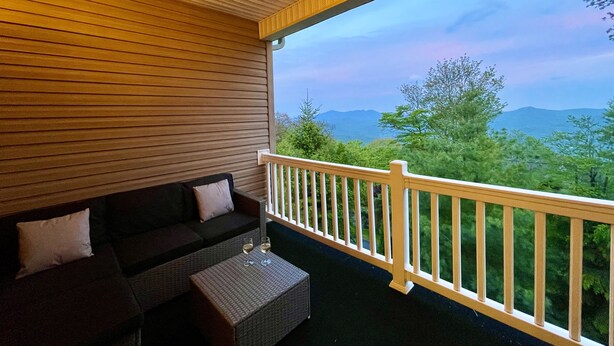Een overdekt balkon met een bank en tafel, met uitzicht op een bergachtig landschap.