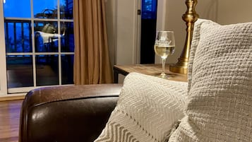 A cozy room with a leather chair, a woven throw pillow, a brass floor lamp, and a glass of wine on a small table.